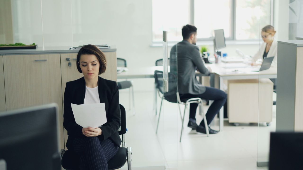 services-04 Business professionals working in a modern office setting with focus on a seated woman.
