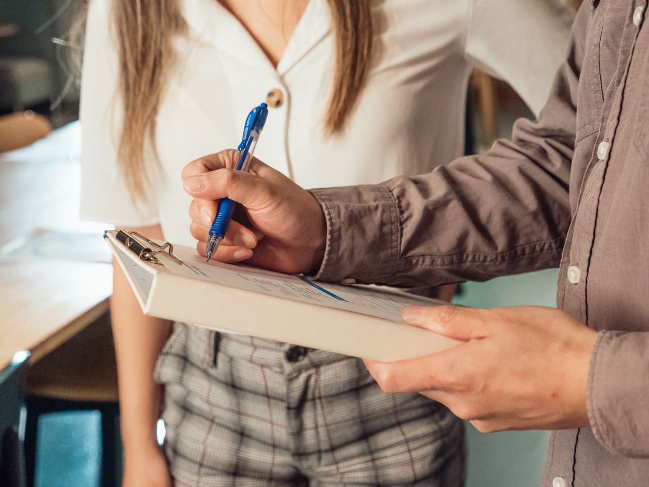A person writing on a clipboard with a ballpen in an office setting.