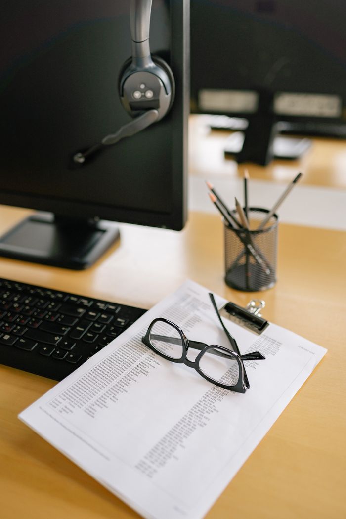 A computer desk featuring a monitor, keyboard, eyeglasses, and documents, perfect for a work setting.